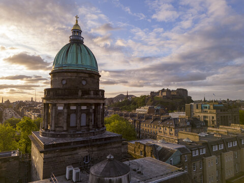 Aerial view of the copper dome of St. George's Tron Church glows softly against the dramatic backdrop of Edinburgh Castle, West End, Scotland, United Kingdom.