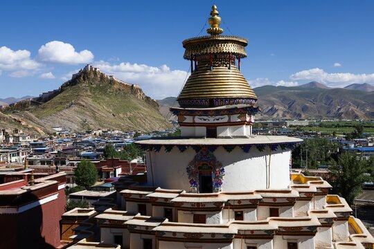 Iconic Kumbum Stupa at Pelkor Ch&ouml;de Monastery in Gyantse, Tibet, with the historic Gyantse Dzong fortress rising on the mountain, showcasing Tibetan Buddhist architecture and heritage.