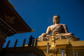 Thimphu, Bhutan - 27 September 2025: View of the majestic Buddha Dordenma statue gleaming gold against the vivid blue sky, framed by traditional Bhutanese architecture.
