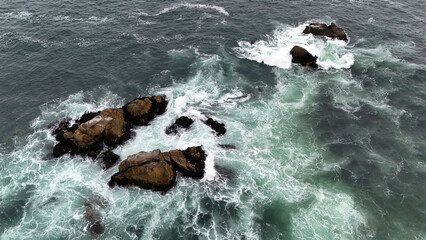 Large ocean waves crashing over dark rocks creating white foam © Prostir Vision