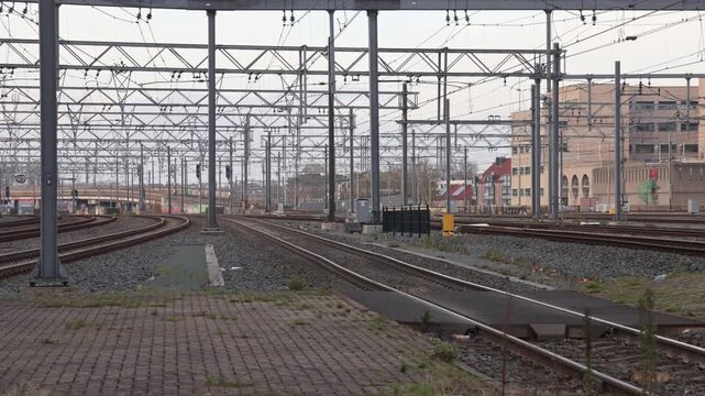 Wide view of Utrecht Central railway yard featuring complex overhead catenary wires and yellow Dutch commuter trains moving on the tracks.