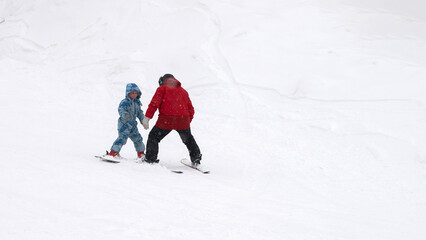 A children's ski instructor conducts a lesson with a child on a gentle snowy slope.