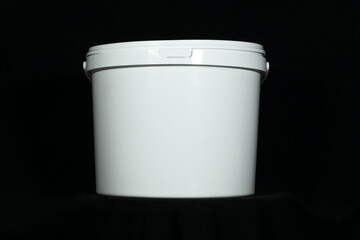 White plastic bucket with lid isolated on black background. Clean white utility bucket with lid and handle on dark backdrop for packaging design cleaning product template or industrial storage concept