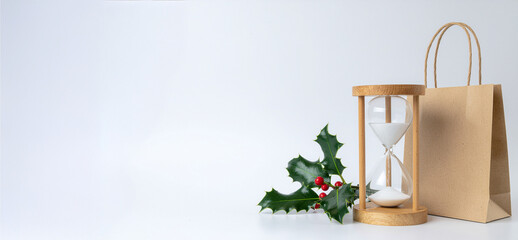 Hourglass Beside a Shopping Bag on White Surface &ndash; Minimalist Christmas Shopping Concept with Copy Space for Seasonal Offers