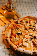 Pizza with cheese, chicken, and mushrooms on a table with oil in the background during evening