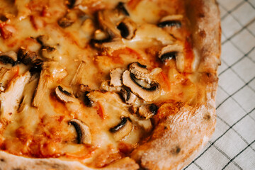 Pizza topped with cheese, chicken, and mushrooms served on a checkered tablecloth during dinner time