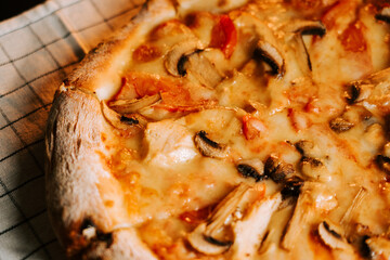 Pizza with cheese, chicken and mushrooms on a checkered cloth at a dining table