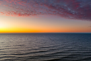 Aerial view of Baltic Sea coast in winter, with bare trees on the cliff and waves rolling under a vivid red sunset sky. Stark northern beauty, elemental in fading light.