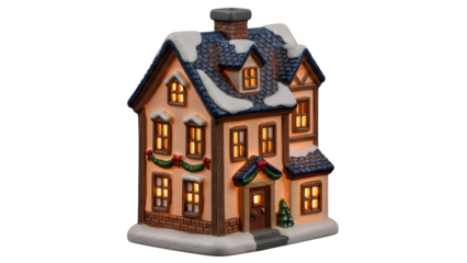 Charming illuminated ceramic Christmas village house with snow dusted roof and festive green garland decoration