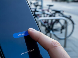 Close-up of a smartphone unlocking screen with a finger interaction. A bicycle is blurred in the background. Modern, blue interface, focus on the unlock gesture