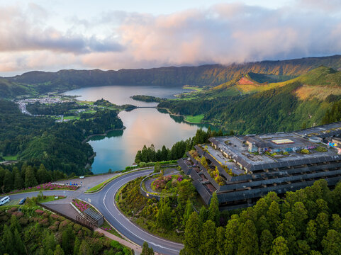 Aerial view of the tranquil Lagoa das Sete Cidades reflecting the sky, nestled amidst vibrant green hills and the iconic Hotel Monte Palace, Sao Miguel, Azores, Portugal.