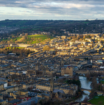 Aerial view of golden sunlight bathing the ancient Roman Baths and the meandering River Avon, casting long shadows across the historic city, Bath, England, United Kingdom.