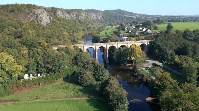 Drone shot of the impressive stone viaduct in Cl&eacute;cy, Normandy, overlooking the Orne River. 4K video with side-view motion. The bridge, framed by autumn trees, creates a picturesque landscape.