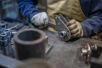 Close photo of the locksmith's table of metal parts for mechanisms. Worker screwing bolt to flat...