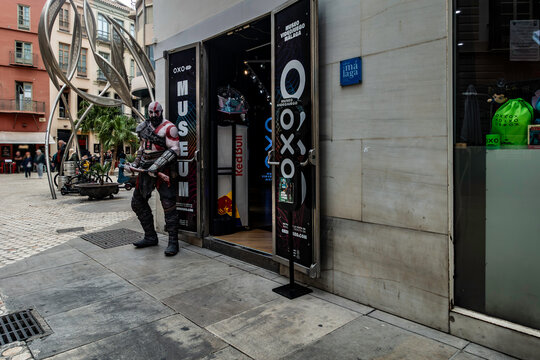 OXO Museo Videojuego Malaga exterior, Kratos cosplayer stands outside. Malaga, Spain, Red Bull banner, gaming museum entrance. Modern art sculpture.