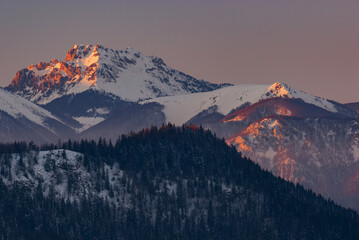 Aerial view of snow-capped mountain peaks kissed by the warm glow of sunrise casting shadows across the landscape, Low Tatras, Zilina Region, Slovakia.