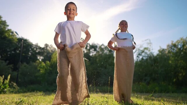 Two boys in field. Children race in sack outdoors. A young girl is playing with a teddy bear in the grass and is very competitive and energetic. A pair of boys in a meadow lifestyle.