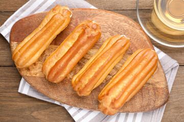 Tasty eclairs and tea on wooden table, flat lay