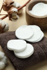 Clean cotton pads, flowers and towel on beige background, closeup