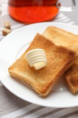 Fresh toasted bread slices with butter and tea on table, closeup