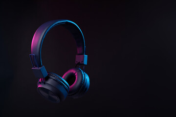 Pair of stylish headphones in air on black background in neon lights, space for text