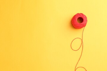Ball of red yarn on yellow background, top view. Space for text