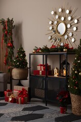 Shelving unit with Christmas decor between small spruce trees near beige wall indoors. Interior design