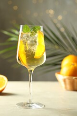 Refreshing spritzer cocktail and oranges on light table against grey background with bokeh effect