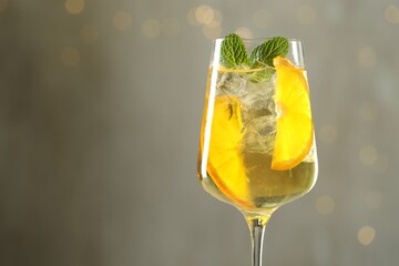 Glass of refreshing spritzer cocktail against grey background with bokeh effect, closeup. Space for text