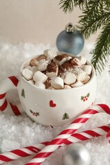 Tasty cocoa with marshmallows, candy canes and Christmas decor on artificial snow, closeup