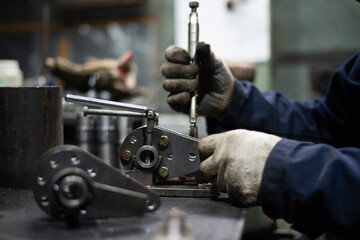 The hands of the master locksmith mount the metal part at the work table in the workshop. Close...