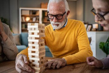 Senior man concentrating on playing jenga game with friends