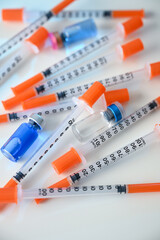 Close up of Pile of Single Use Syringes with Orange Safety Tips and Glass Vials