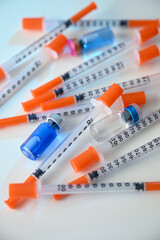 Close up of Pile of Single Use Syringes with Orange Safety Tips and Glass Vials