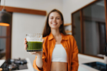 Smiling young woman holding a glass of green smoothie in a bright kitchen, promoting healthy eating and wellness with vibrant colors