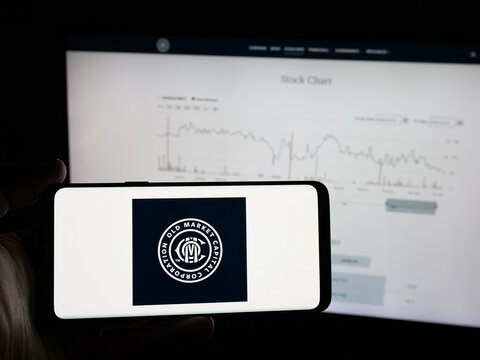 Stuttgart, Germany - 12-02-2025: Person holding smartphone with logo of company Old Market Capital Corporation on screen in front of website. Focus on phone display.