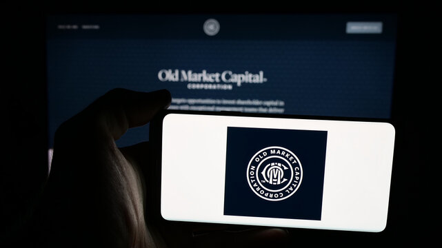 Stuttgart, Germany - 12-02-2025: Person holding mobile phone with logo of company Old Market Capital Corporation on screen in front of web page. Focus on phone display.