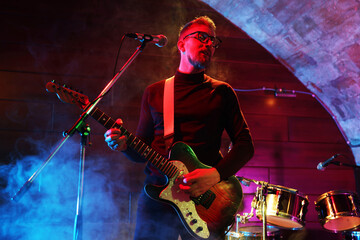 Man playing electric guitar on stage with smoke, low angle view