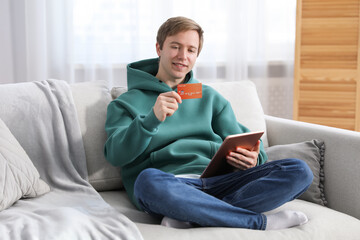 Young man making online payment with tablet and credit card indoors