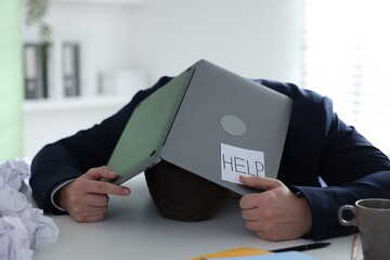 Man with laptop and sign Help at table in office