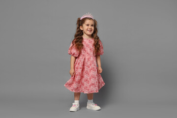 Smiling little girl in headband and dress on grey background