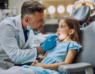 Fototapeta premium A child during a dental visit. The girl sits in the dental chair with her mouth open while the dentist checks her teeth.