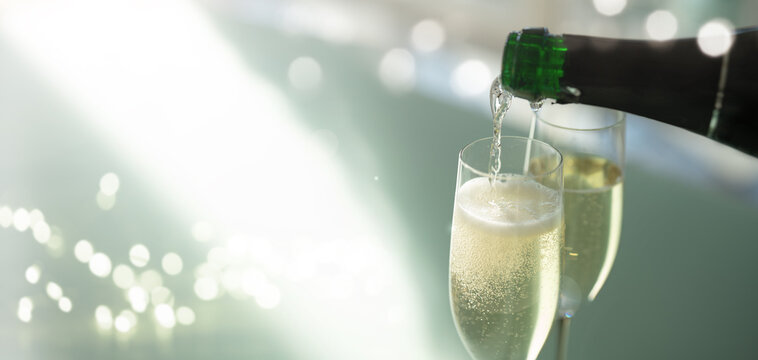 Pouring champagne into glasses. Bottle of sparkling wine against an elegant, modern light green background with a soft bokeh. Celebrating with flowing golden drink.