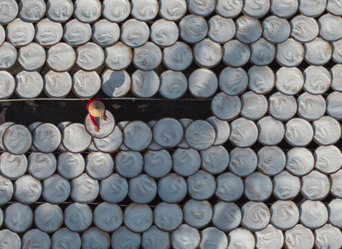 Aerial view of a person wearing a conical hat walking on a dark path surrounded by stacks of dried rice paper under the sun, Tay Ninh, Tay Ninh, Vietnam.