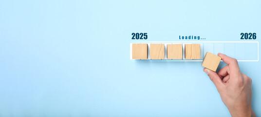 New Year 2026. Man putting wooden cube next to others onto loading bar on light blue background, top view