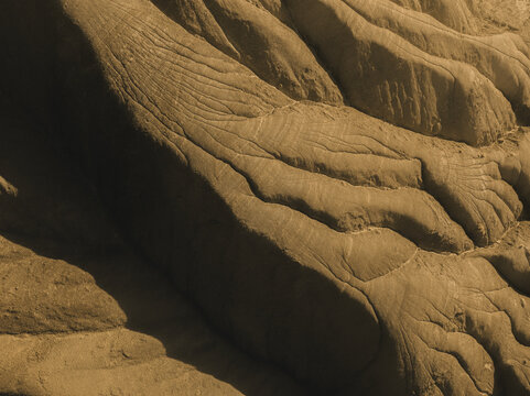 Aerial view of undulating, arid badlands carved by time and weather into a textured, monochromatic landscape of shadows and light, Centuripe, Sicilia, Italy.