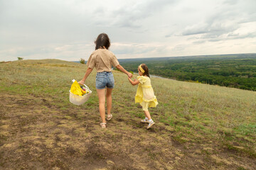 Family on a meadow, mother and daughter holding hands while carries picnic basket