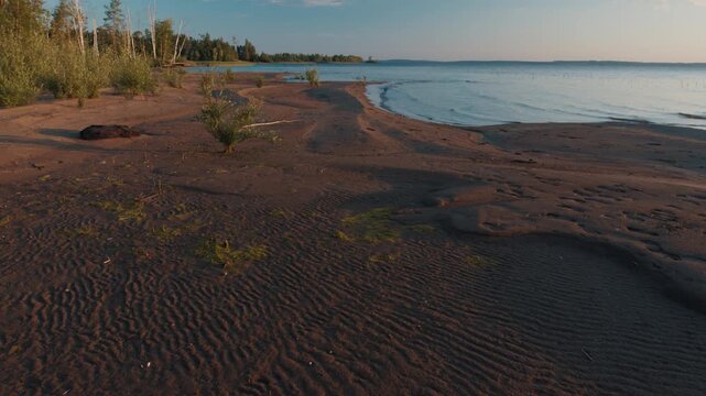 Wild beach of the lake with gentle calm waves during sunset