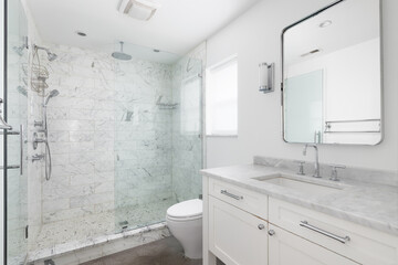 A bright and modern white bathroom featuring a spacious glass-enclosed shower with marble tile and...