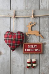 A Christmas holiday arrangement featuring a red plaid heart pillow, a small wooden reindeer cutout, a framed "MERRY CHRISTMAS" sign, and three miniature hanging stockings, all set against a rustic whi